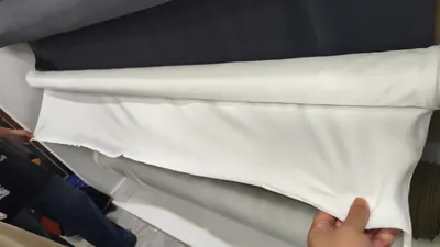 Kéo căng một khổ vải trắng để xem bề mặt tại cửa hàng trong chợ vải, 5/2026.